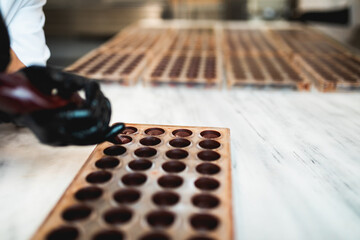 Professional confectioner pouring melted black chocolate into silicone mold.