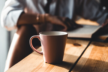 Woman in the morning drinks coffee and reads old book in a white shirt. Education, drink. manicure