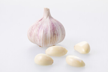 Unpeeled garlic bulb closeup with peeled garlic cloves around it on a white background 