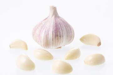 Unpeeled garlic bulb closeup with peeled garlic cloves around it on a white background 