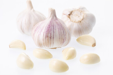 Unpeeled garlic bulb closeup with peeled garlic cloves around it on a white background 