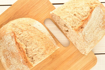 Two halves of a fragrant loaf without yeast with cereal with bran on a bamboo board, close-up, on a white wooden table.