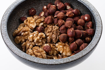 Peeled walnuts and hazelnuts in a grey, handmade bowl on white 