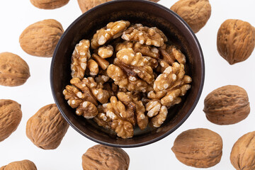 Peeled walnuts in a little brown bowl shot from the top on white background 