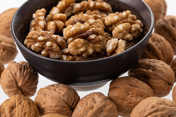 Peeled walnuts in a brown bowl with unpeeled walnuts around it 