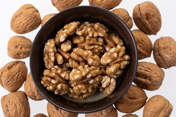 Peeled walnuts in a little brown bowl shot from the top on white background 