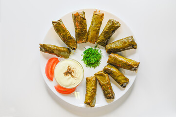 Top view of Lamb wrapped in grape leaves. Dolma with sauce and vegetables on a white plate. 