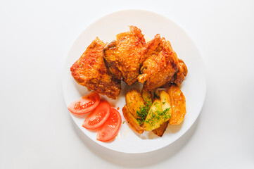 Top view of Pieces of fried chicken with fried potatoes and tomatoes on a white plate.