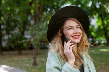 Portrait of a beautiful woman with braces wearing a hat and coat talking on the phone outdoors