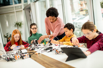 Happy kids with their African American female science teacher with laptop programming electric toys and robots at robotics classroom