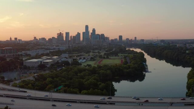 A busy highway (Mopac)  near Downtown Austin bustles as the day starts, as a gorgeous sunrise lights up the skyline and lake Austin in the background