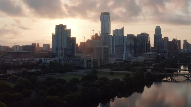 Sweeping Aerial during a summer sunrise over downtown Austin, TX, as the camera sweeps over lady bird lake, with reflections glowing off of the water, reverse movement.