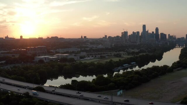 A busy highway (Mopac) near Downtown Austin bustles as the day starts, as a gorgeous sunrise lights up the skyline and lake Austin in the background
