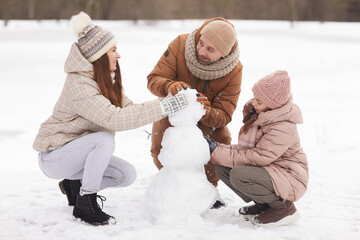 Full length portrait of happy family building snowman together while enjoying walk outdoors in...
