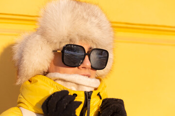 Portrait of a happy woman with a smile in snow-white zabas in winter against a yellow wall on a sunny day in a warm Russian Siberian hat