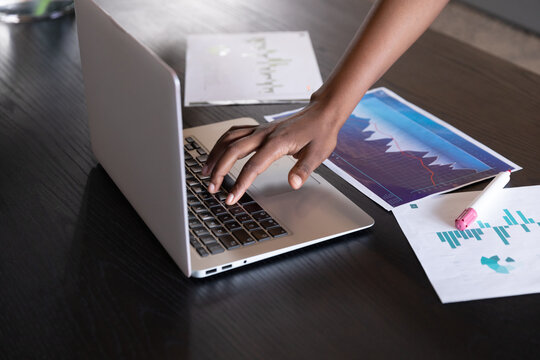Mixed race businesswoman standing using laptop going through paperwork in modern office