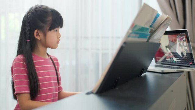 Asian young girl learning piano lesson online at home by e-learning.