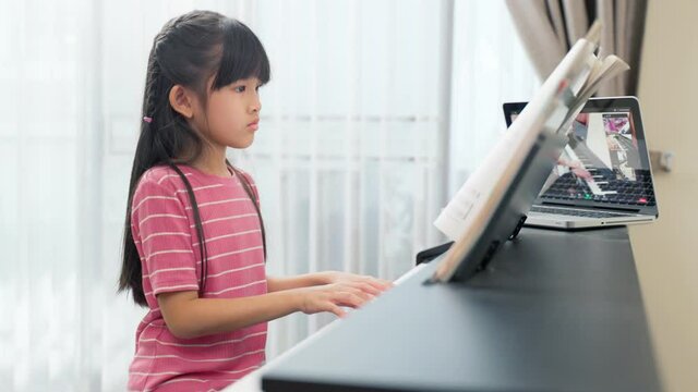 Asian young girl learning piano lesson online at home by e-learning.
