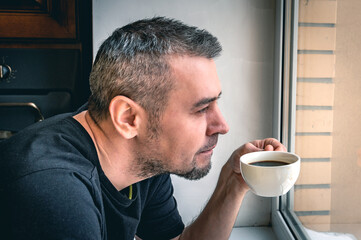 Close up of a bearded man drinking coffee. Portrait of a man enjoying a cup of tea in front of a sunlit window.