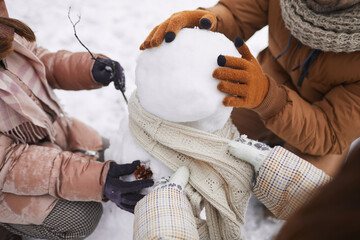 Close up of unrecognizable happy family building snowman together while enjoying winter vacation outdoors