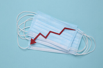 Facial medical masks and a falling arrow on a blue background. Decrease in covid-19 infection statistics