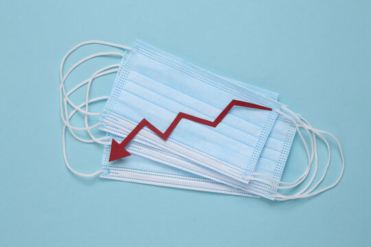 Facial medical masks and a falling arrow on a blue background. Decrease in covid-19 infection statistics