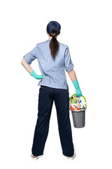 A girl in the uniform of a cleaning lady and a baseball cap is standing back on a white background with a plastic basket with wet cleaning products