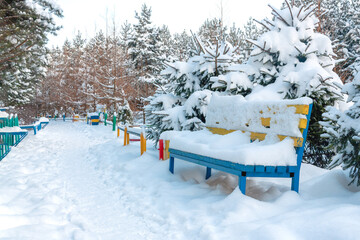 Bench covered with a thick layer of snow in the park near the path
