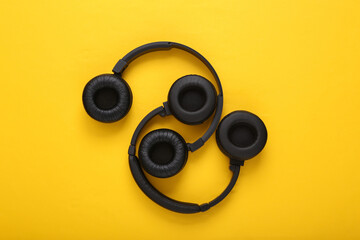 Two pairs of black wireless stereo headphones on yellow background. Top view
