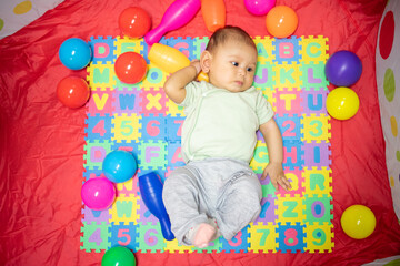 Fototapeta na wymiar 3-4 Month Old Baby GIrl lying on play mat playing with colored toys developing her eyes and motor skills, young baby girl grasping and holding her toys
