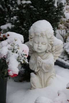 Friedhofsengel neben Blumen mit Schnee bedeckt im Winter