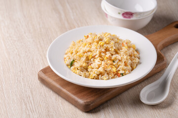 Chinese fried rice in white plate on bright wooden table background.