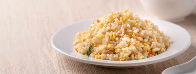 Chinese fried rice in white plate on bright wooden table background.
