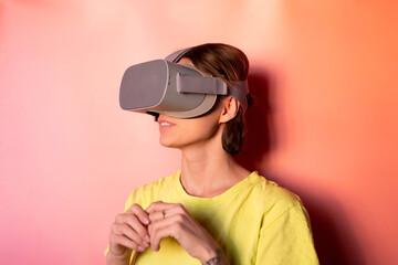 Emotional portrait of woman in virtual reality glasses in studio on pink orange background