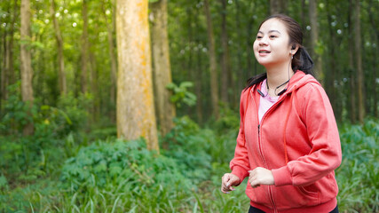 Fototapeta premium Asian woman running in forest wearing jacket and earphone