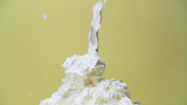 Whipped cream can spraying into large pile panning down follow slow motion with yellow studio backdrop