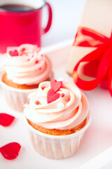 Valentines cupcake cream cheese frosting decorated with heart candy, mug of coffee and gift box on the background.