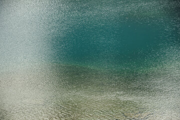 Texture of green blue calm water of lake. Meditative ripples on water surface. Nature minimal background of green blue lake with golden shine. Natural backdrop of lake fragment with clear azure water.