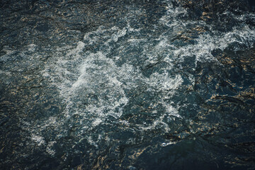 Atmospheric nature background of golden water of mountain river in sunrise or sunset. Scenic fragment of water surface with gold sunshine reflection. Sunlight reflected in golden blue water stream.