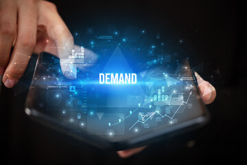 Businessman holding a foldable smartphone with DEMAND inscription, business concept