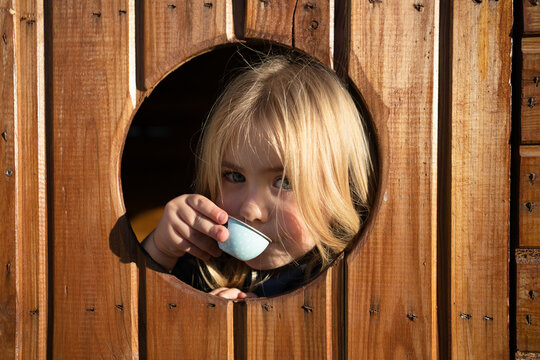 Ni&ntilde;a rubia bebiendo una taza de caf&eacute; asomada a la puerta de su casa de madera