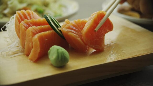 Picking Salmon Sushi Using Wooden Chopsticks And Dipping On Soy Sauce. - close up