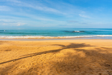 View of coconut tree shadow, blue sky, blue sea, small wave and yellow sand that is signature of beautiful seascape scene at Phuket Province, Thailand in the morning of holiday.