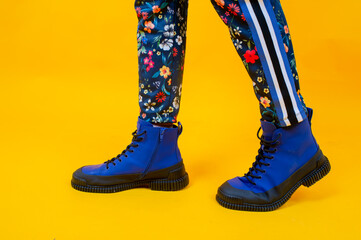 Fashion woman's legs in colorful pants and blue boots over yellow background