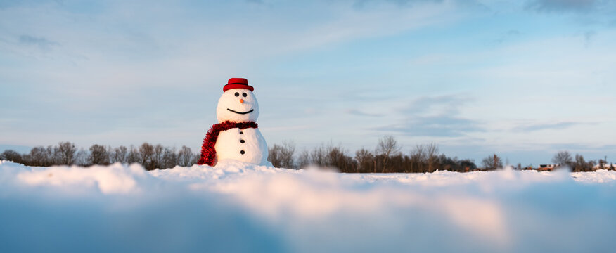 Funny snowman in stylish red hat and red scalf on snowy field. Panoramical photo ideal for site head mockup