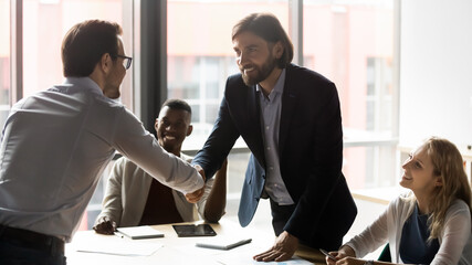 Happy two caucasian businessmen in formal wear shaking hands, establishing partnership at office...