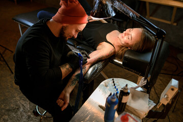 Obraz na płótnie Canvas Professional male bearded caucasian tattoo master is working in cozy atmospheric studio