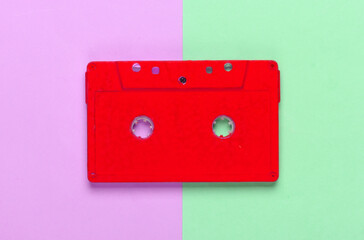 Red audio cassette on pink green background. 80s. Top view