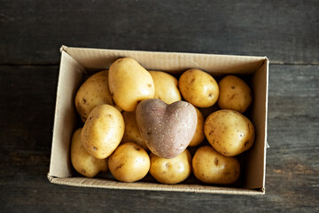 Red potato in the shape of a heart in a cardboard box among white potatoes.