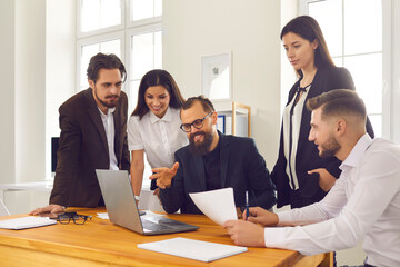 Smiling business people team sitting in office around laptop and discussing startup